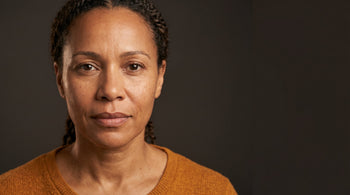 52-year-old African Australian woman with olive skin in a warm-lit portrait, showing healthy skin texture and a calm, confident expression