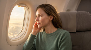 Traveller with healthy glowing skin seated by an aircraft window with a small skincare kit on the tray table