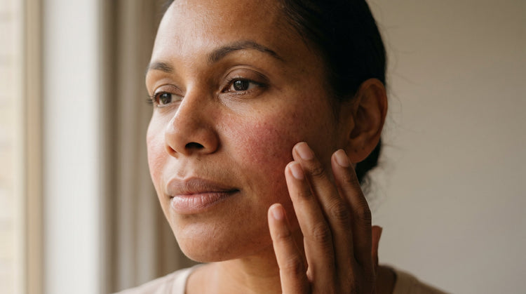 40-year-old African Australian woman with olive skin gently touching her cheek, looking thoughtful, soft natural light highlighting skin texture
