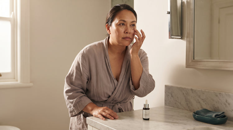 Woman with olive skin examining her undereye area in a bathroom mirror in natural morning light